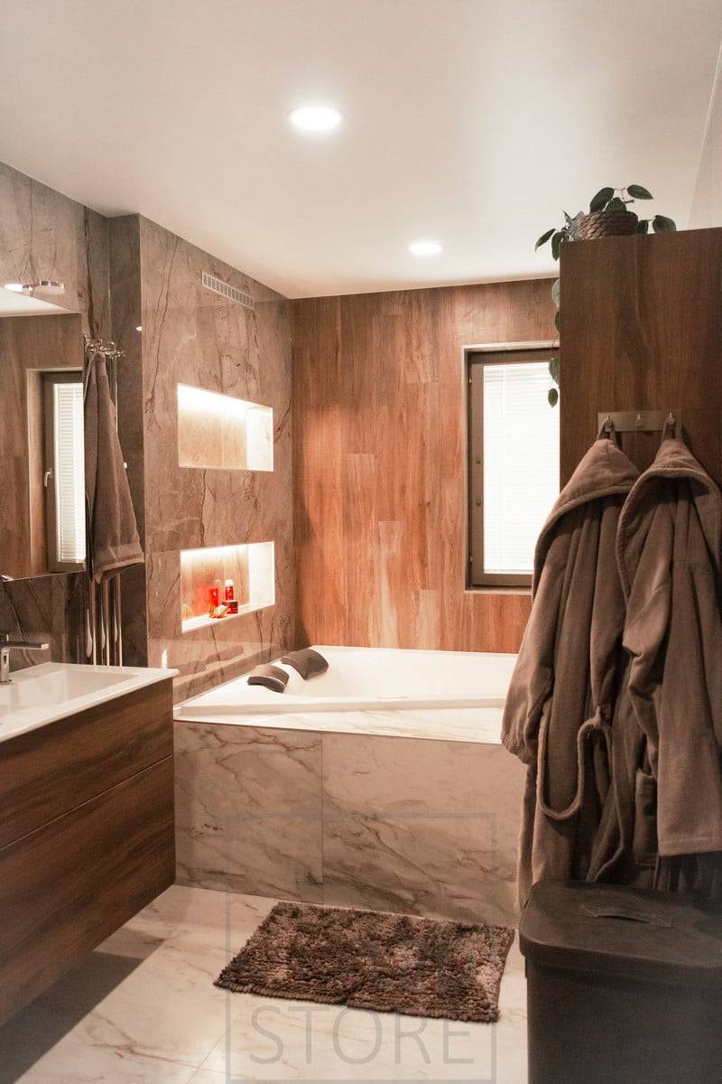 Salle de bains avec dalles de plafond à leds au plafond. La lumière émise par le luminaire est plus uniforme que celle d'un spot et est idéale pour l'éclairage général. Les bandes LED sur les étagères à shampooing apportent une lumière d'ambiance supplémentaire. Ledstore.fi